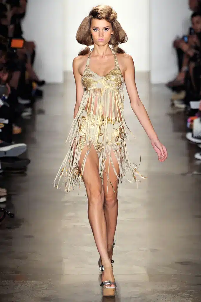 A model walks the runway in a fringed dress.