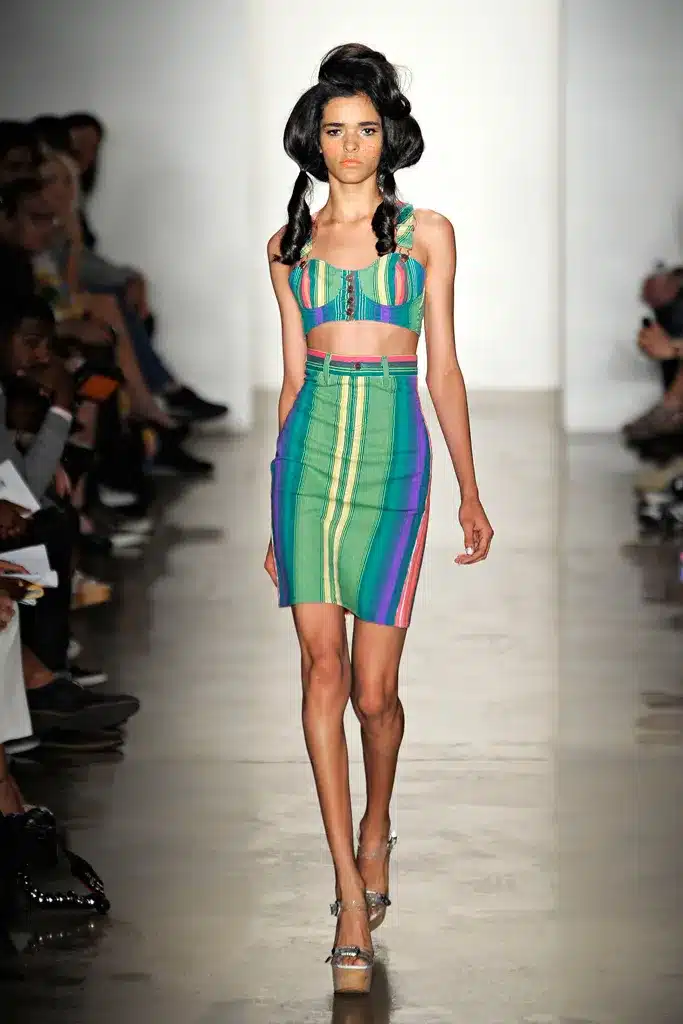 A model walks the runway in a rainbow striped outfit.