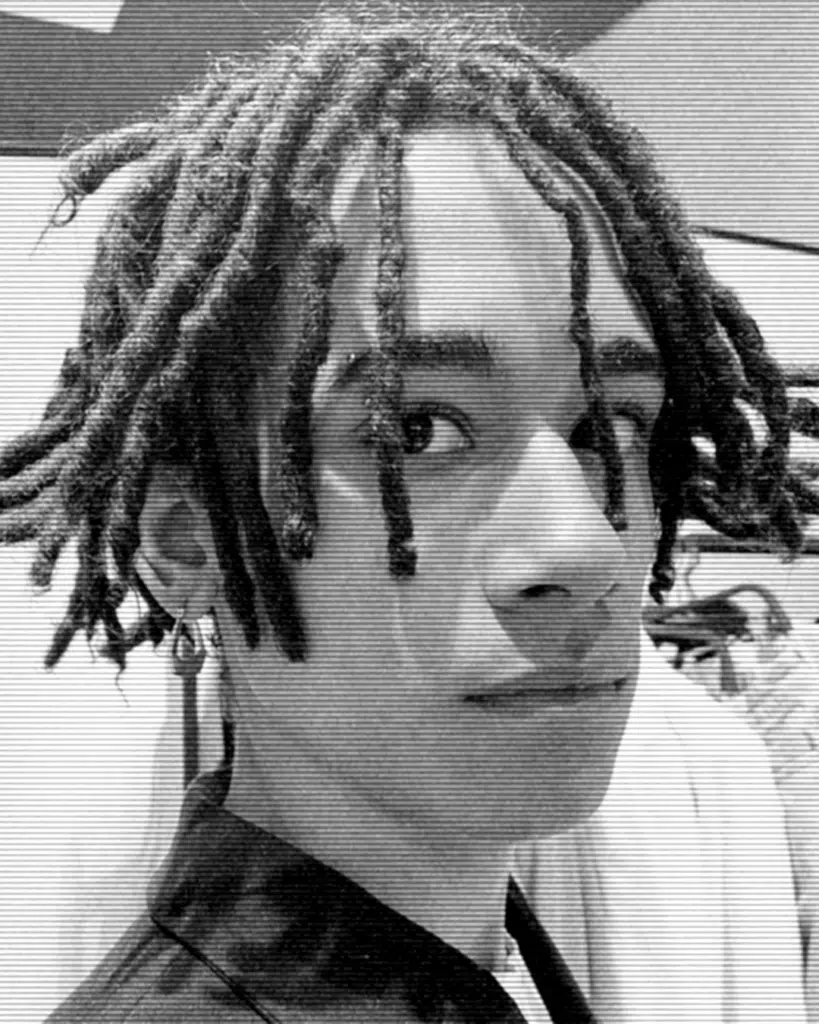 A man with dreadlocks is looking at the camera.