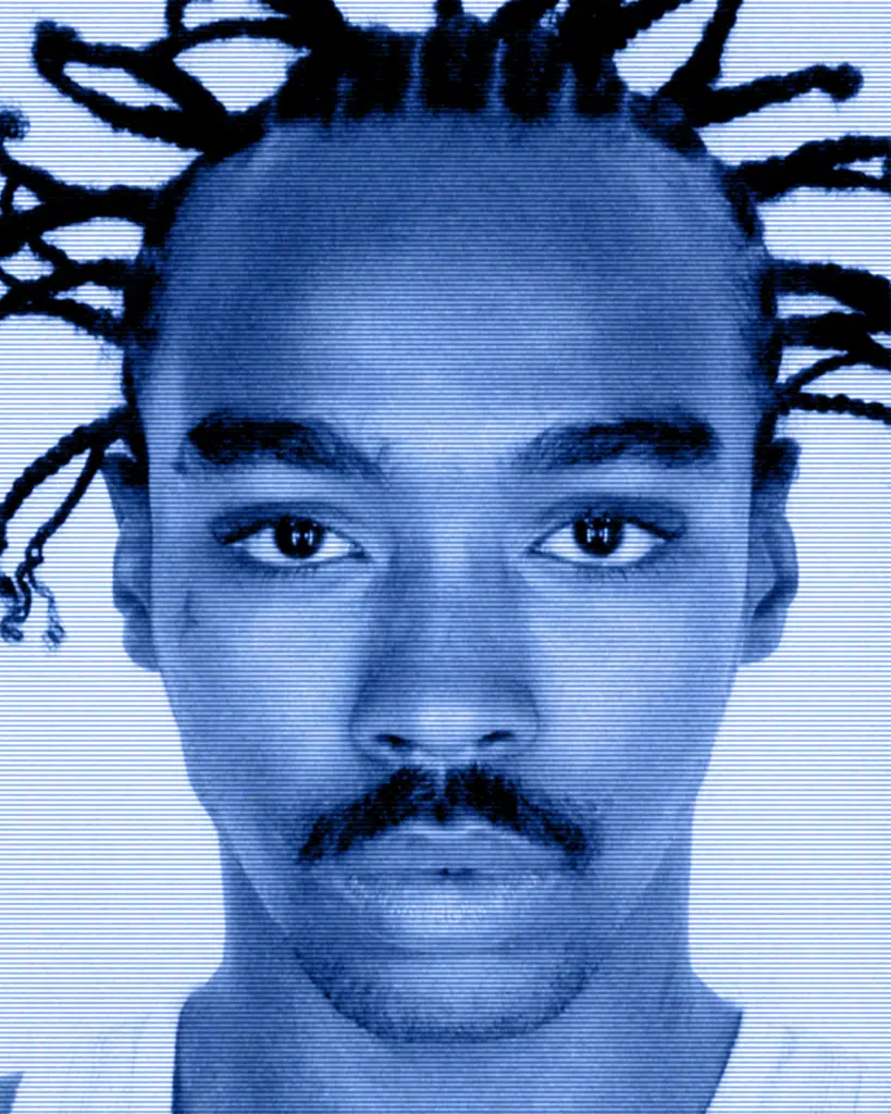 A man with dreads and mustache is looking at the camera.