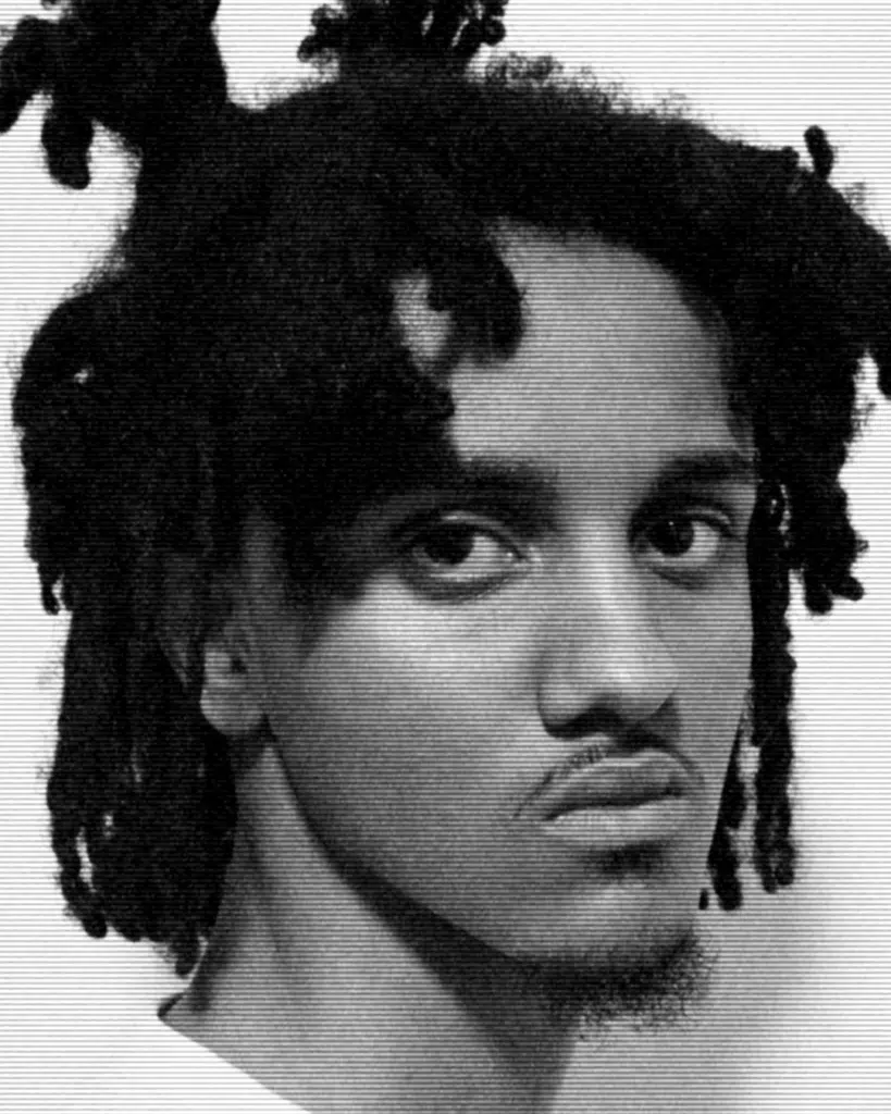 A man with dreadlocks is looking at the camera.