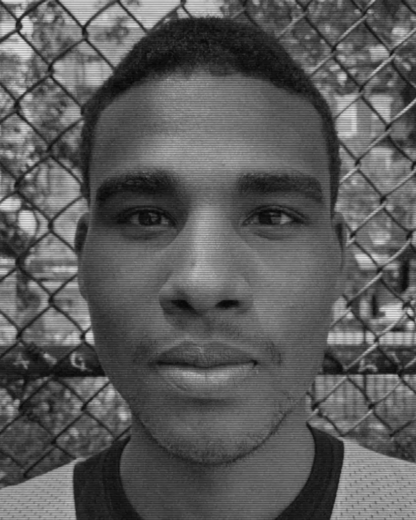 A black and white photo of a man in front of a fence.