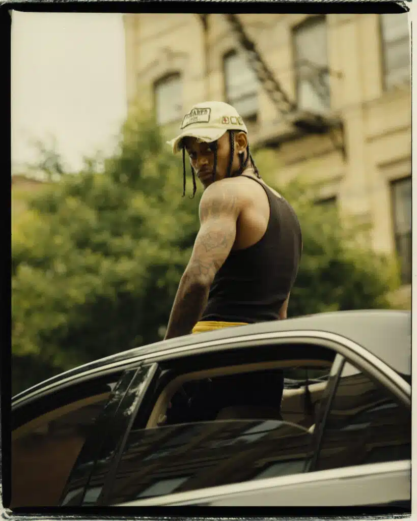 A man with long hair and a hat on top of his car.