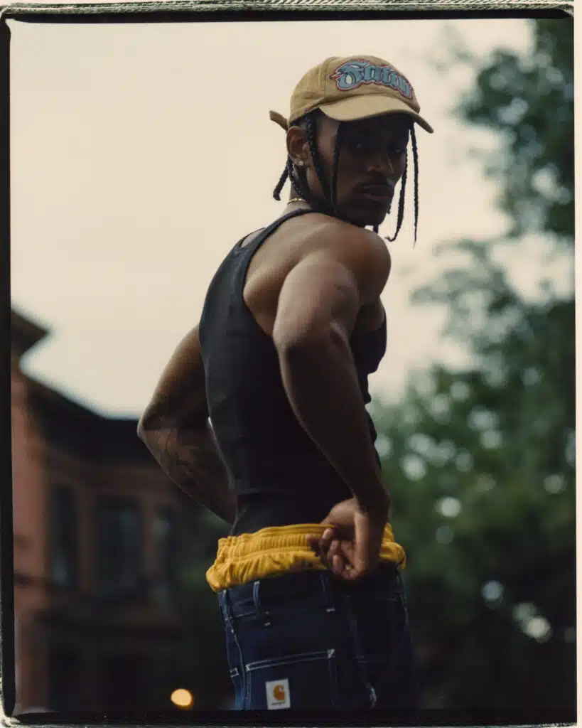 A man in black shirt and yellow hat standing next to building.