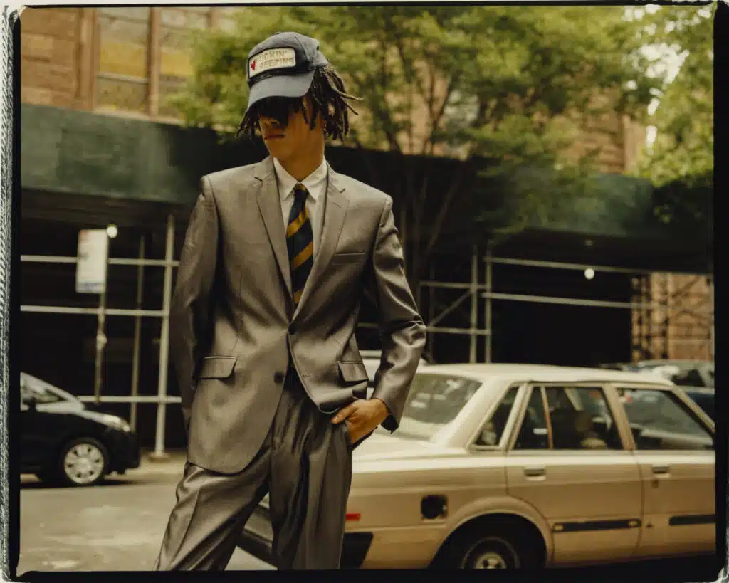 A man in a suit and hat standing next to a car.