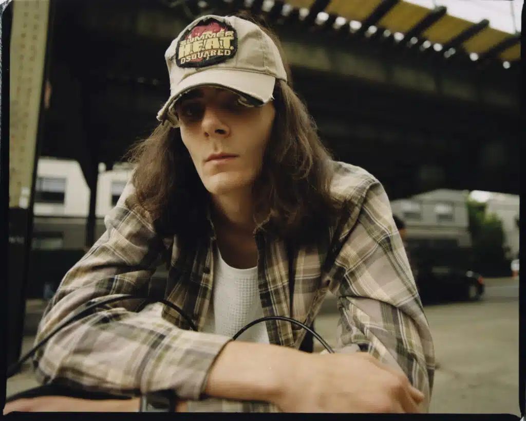 A man in plaid shirt and hat sitting on the ground.