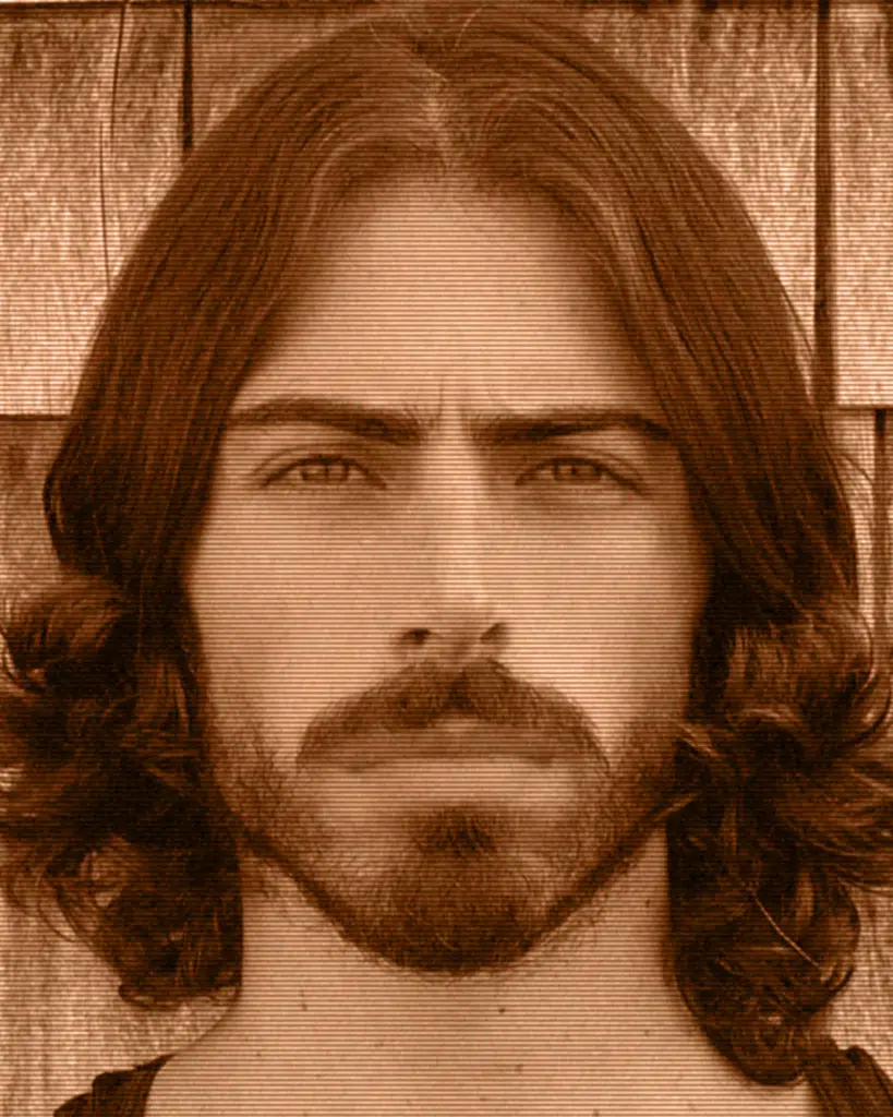 A man with long hair and beard is looking at the camera.