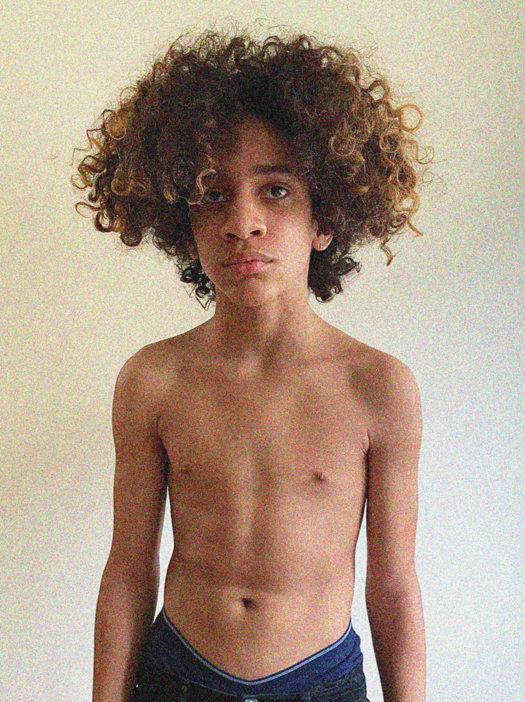 A young boy with curly hair is posing for the camera.