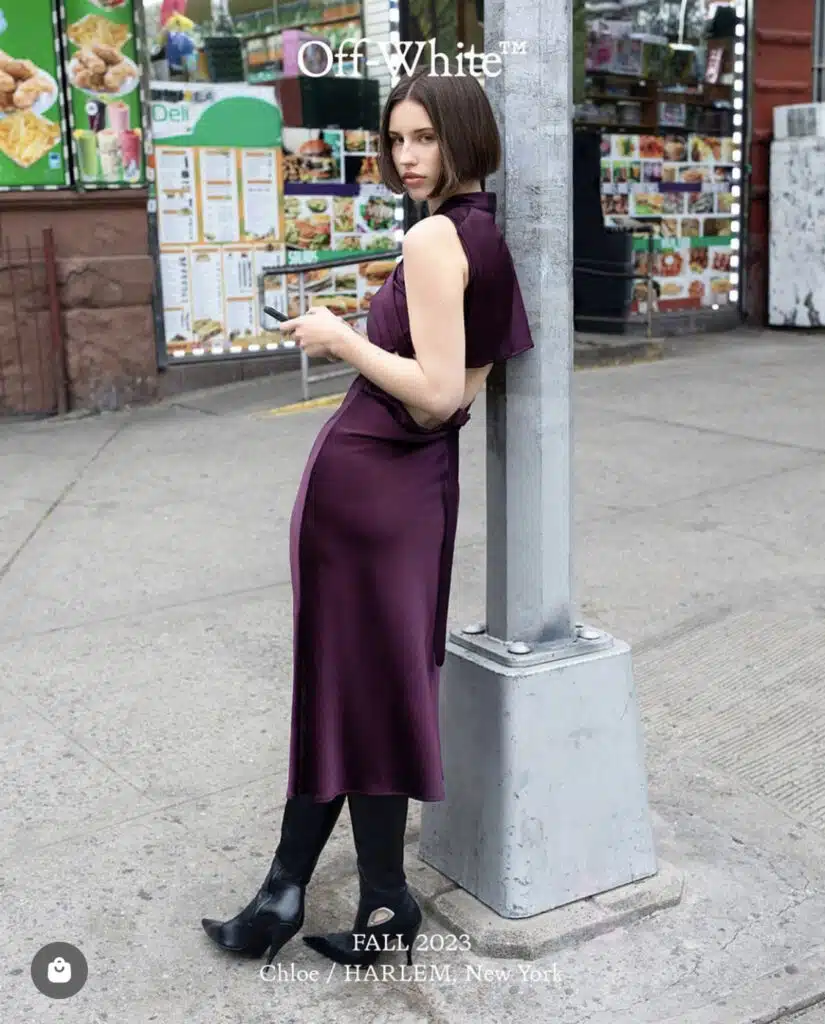 A woman in purple dress leaning on pole.