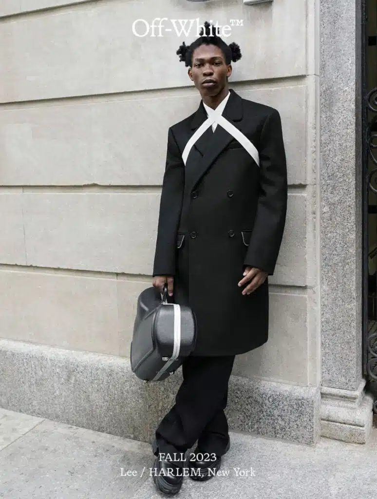 A man in black coat holding a hat and bag.