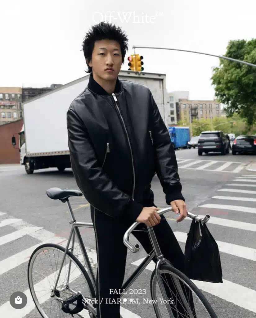 A man in black jacket holding a bike on street.