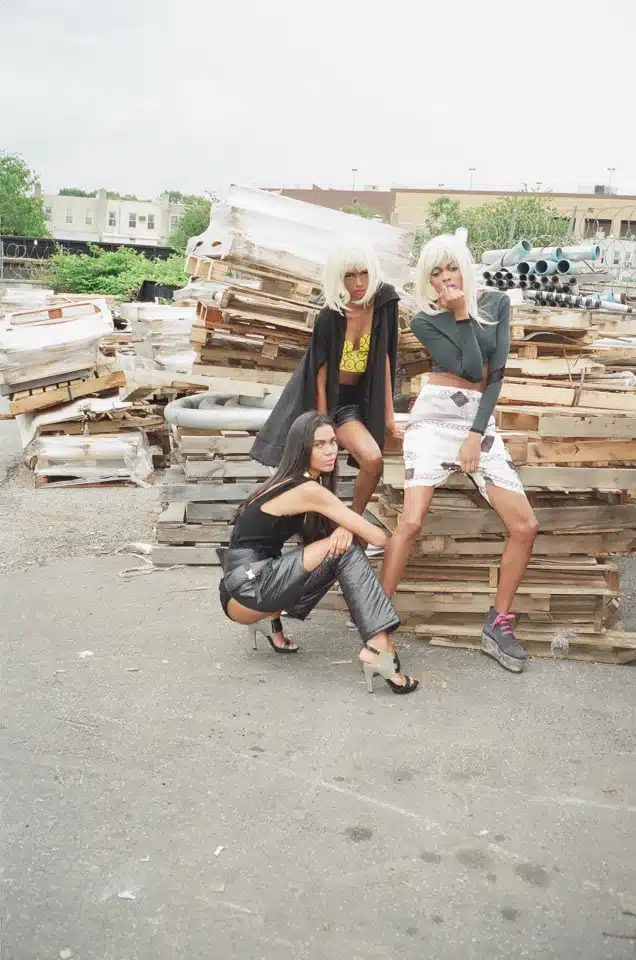 Three women posing for a picture in front of stacks of wood.