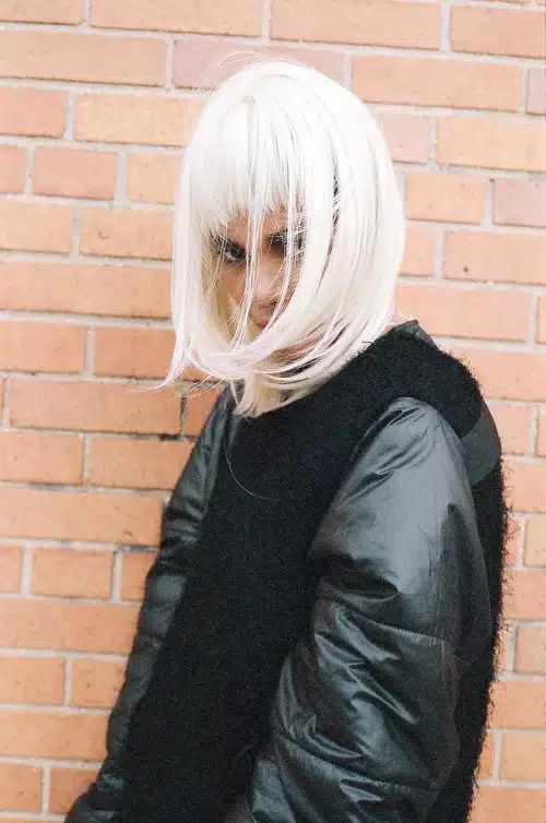 A woman with white hair standing in front of a brick wall.