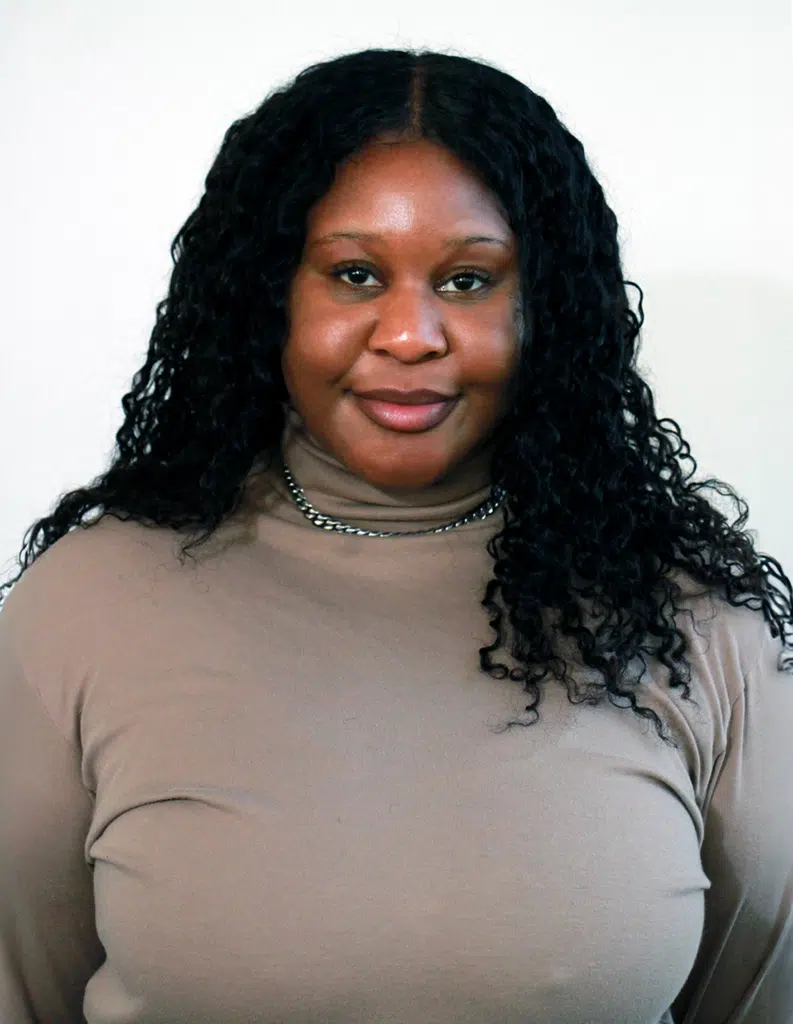 A woman with long black hair wearing a tan shirt.