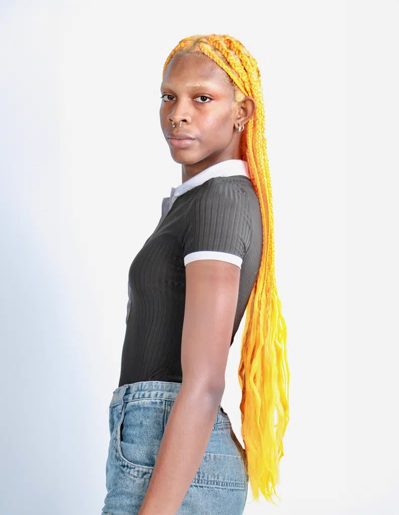 A woman with long yellow hair standing in front of a white wall.