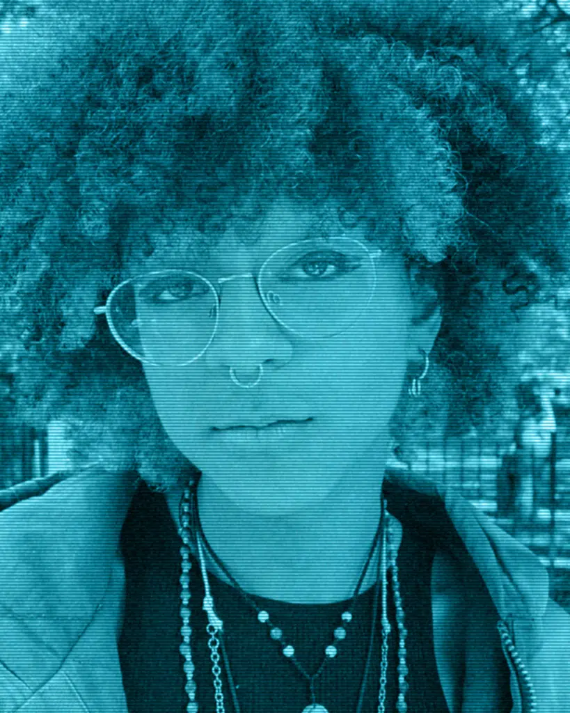 A woman with curly hair and glasses is posing for the camera.