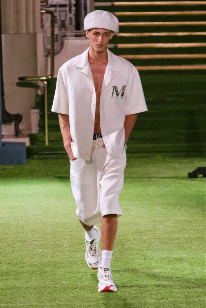 A man in white shirt and shorts walking on grass.