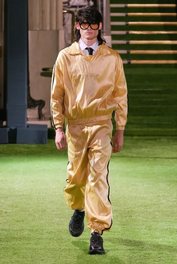 A man in yellow suit and tie walking on grass.