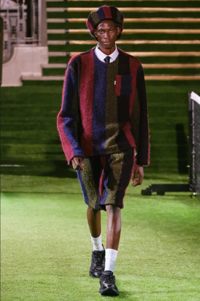 A man in striped shirt and shorts walking on grass.