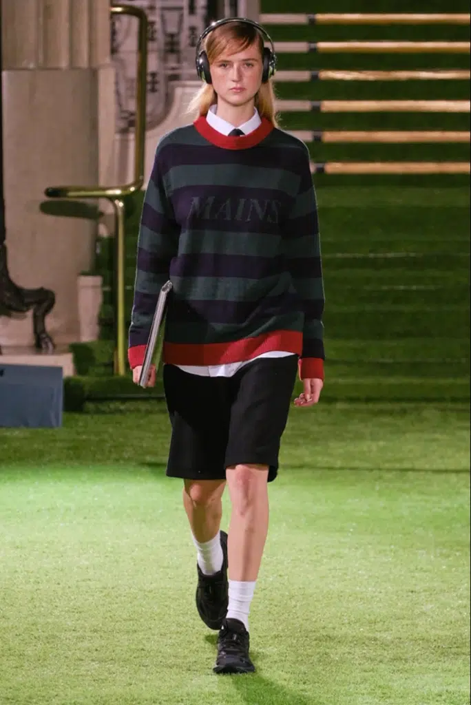 A man in shorts and sweater walking on the grass.