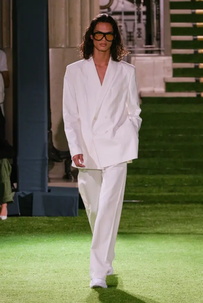 A woman in white suit walking on grass.