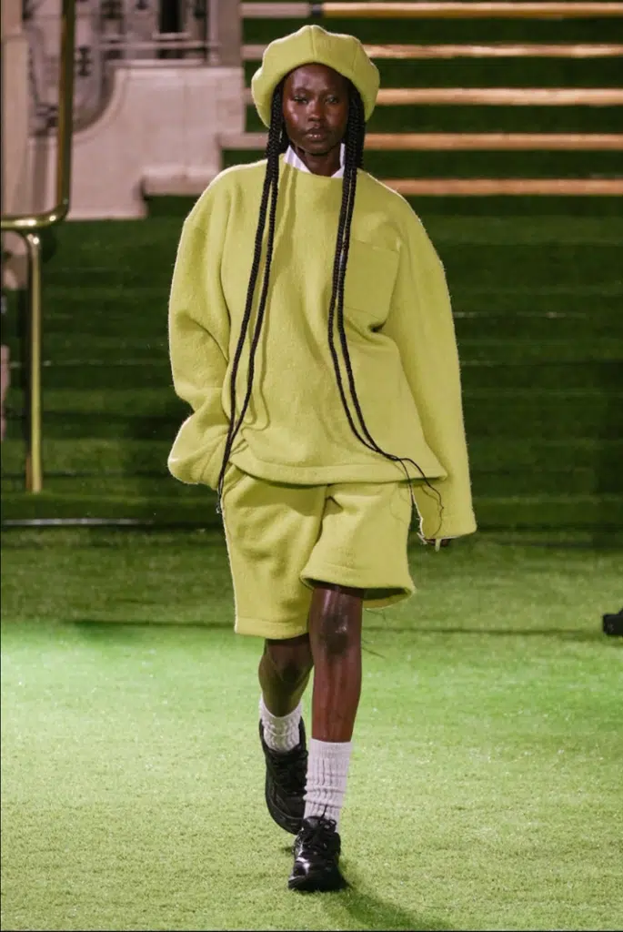 A man in yellow shorts and sweater walking down the runway.