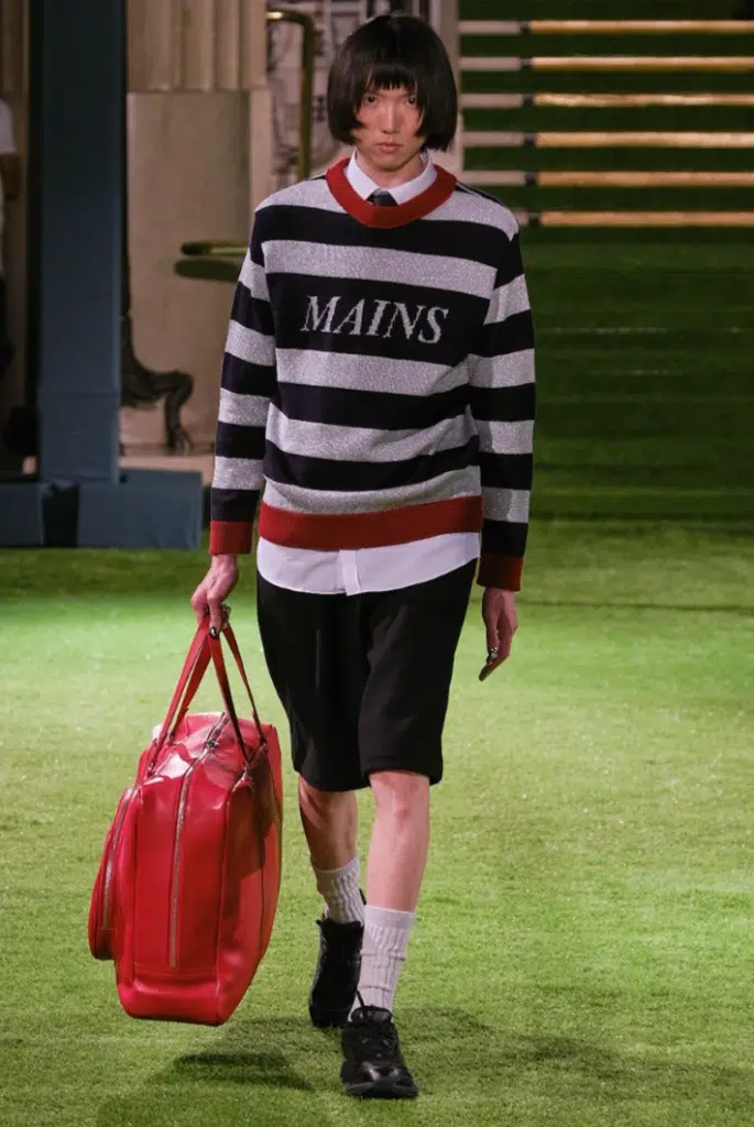 A man in shorts and striped sweater carrying luggage.