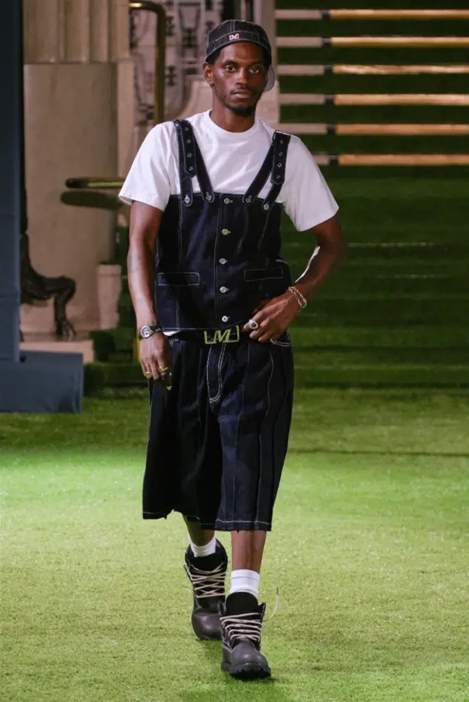 A man in overalls is walking on the grass.