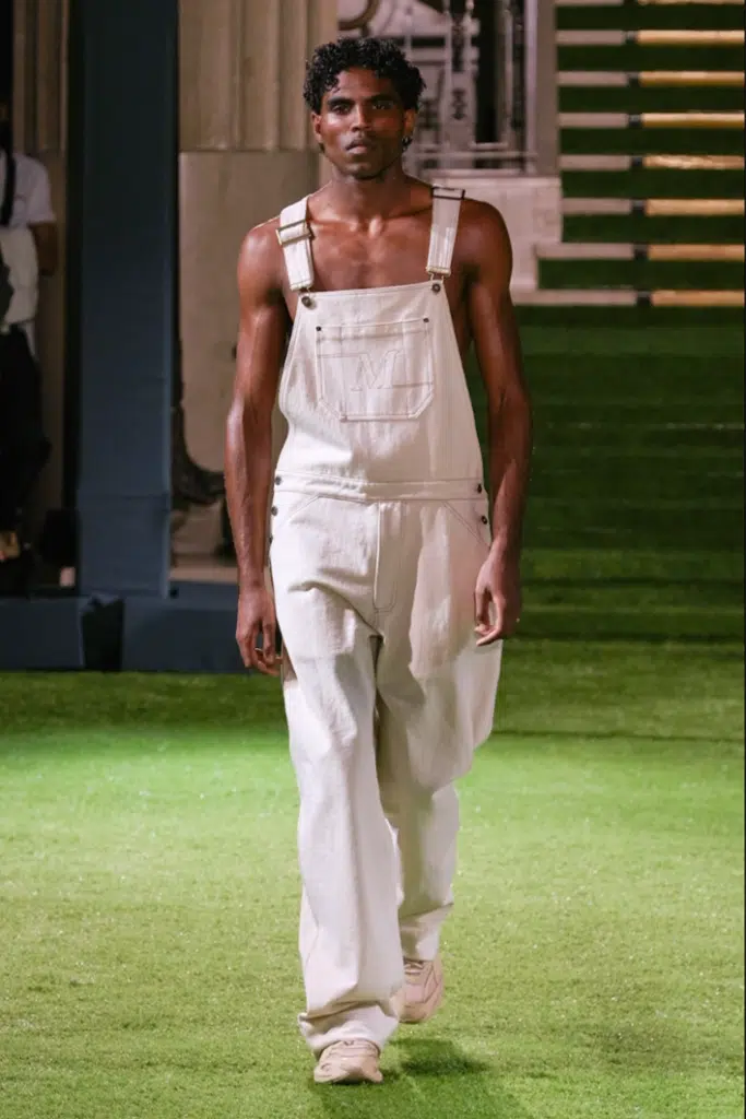 A man in white overalls is walking on the grass.