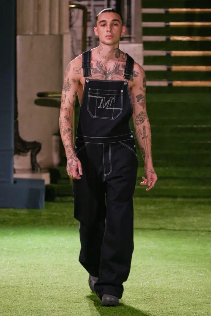 A man with tattoos is walking on the grass.