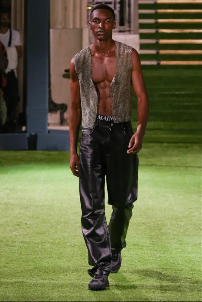 A man in leather pants and vest walks down the runway.