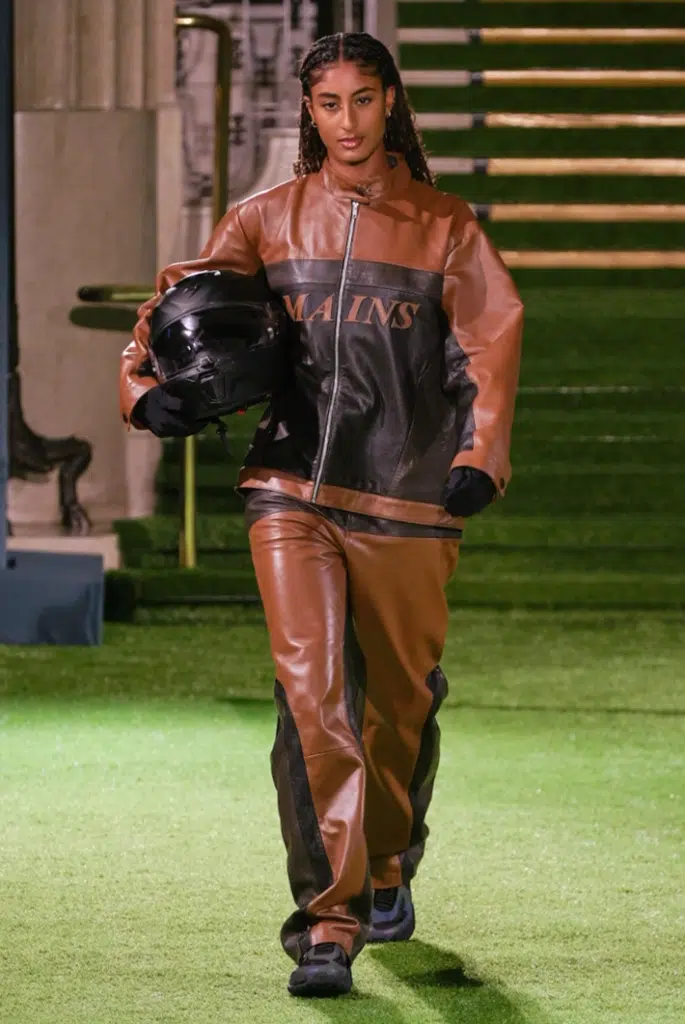 A man in brown and black outfit holding helmet.