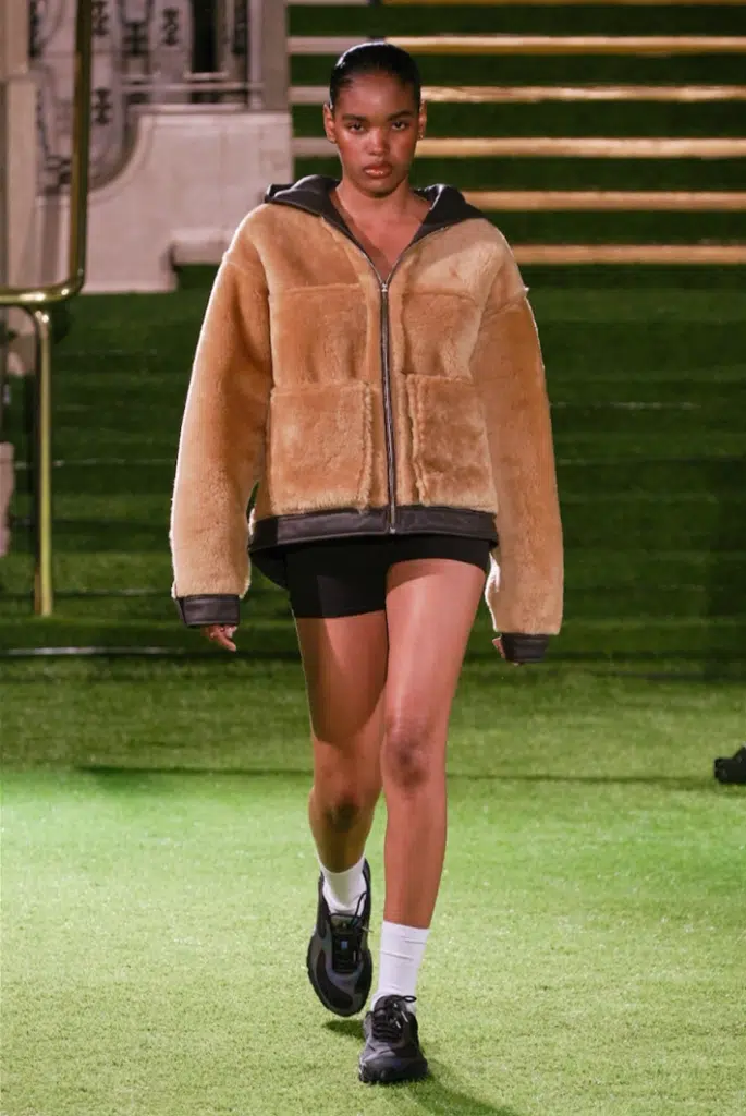 A woman walking down the runway wearing shorts and a jacket.