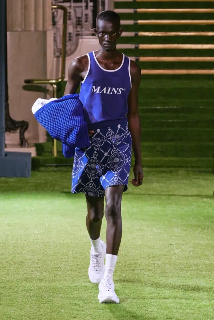 A man in blue shirt and shorts walking on grass.