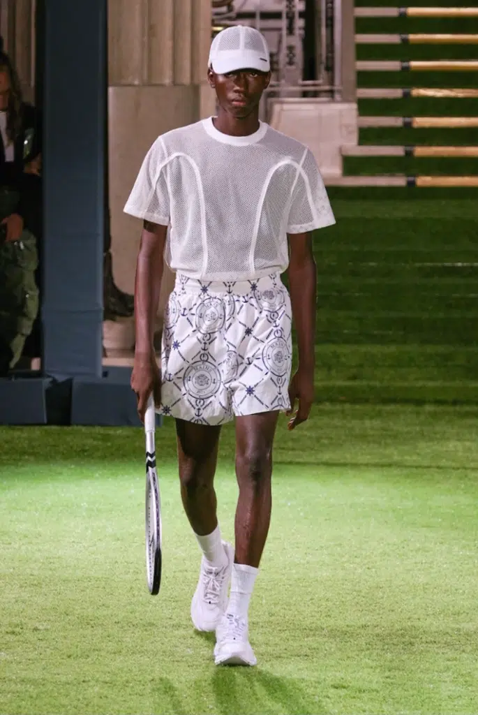 A man in white shirt and shorts holding a tennis racket.