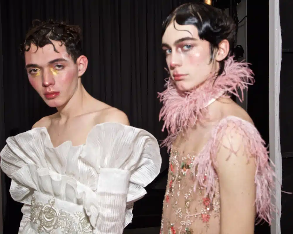 Two men in white and pink outfits one has a feather boa.