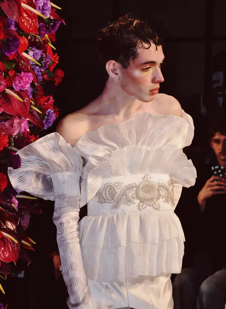 A man in white dress standing next to flowers.