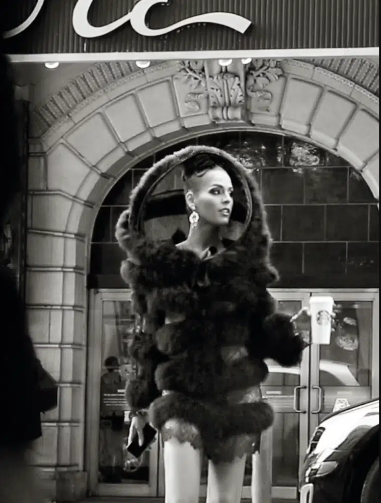 A woman in fur coat standing outside of building.