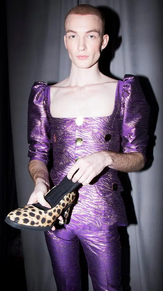 A woman in purple dress holding onto leopard print shoe.