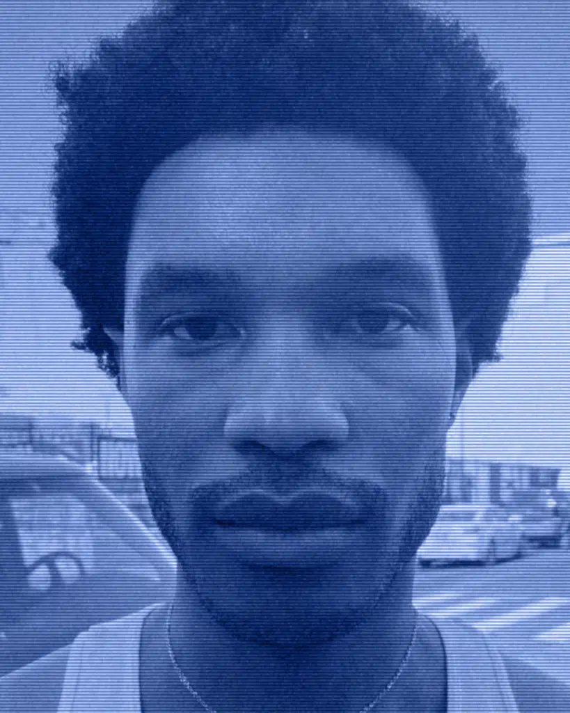 A man with a beard and afro is standing in front of a car.