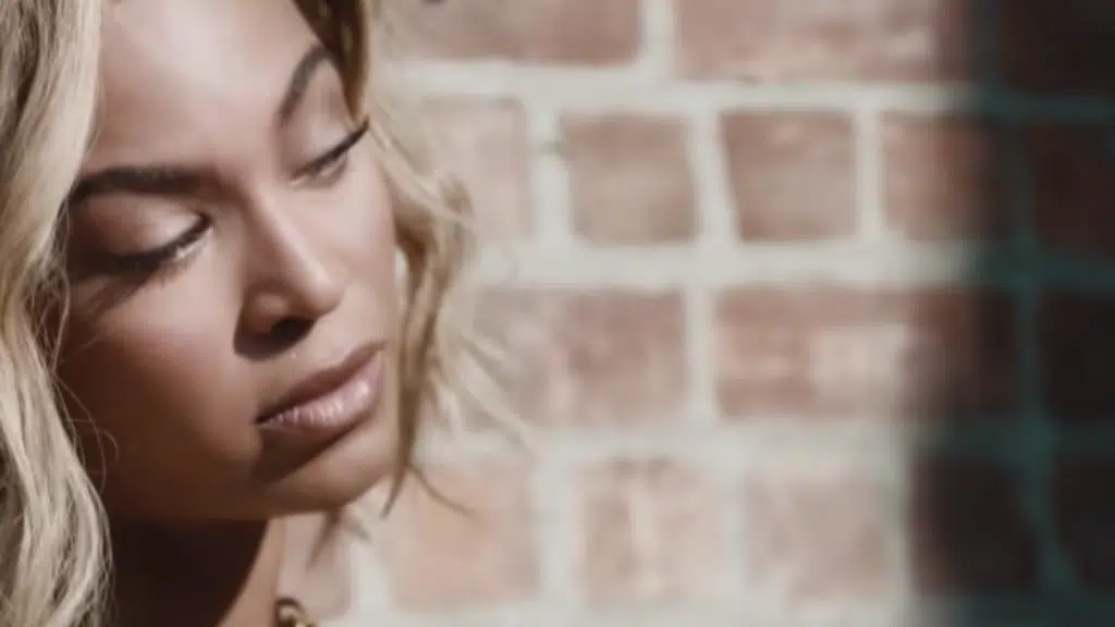 A woman with her eyes closed in front of a brick wall.