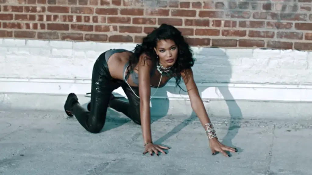 A woman in black leather pants and top crouching on the ground.