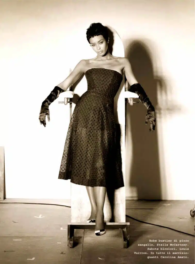 A woman in black dress and gloves standing on white pedestal.