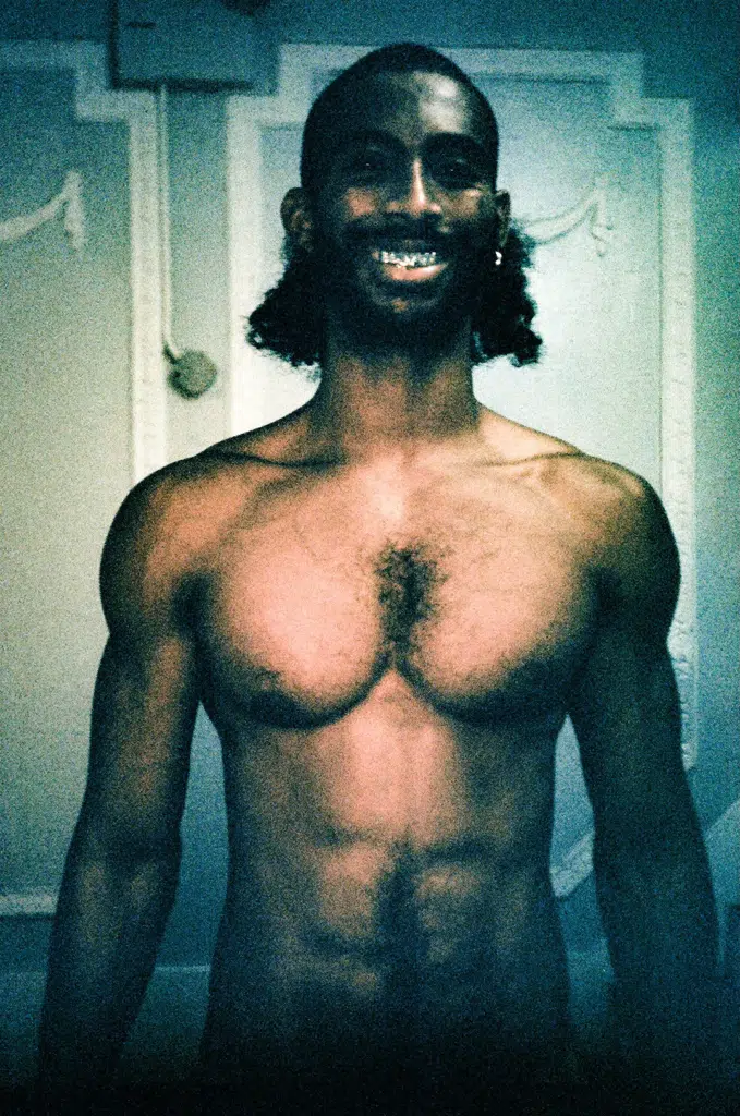 A man with no shirt and beard smiling for the camera.