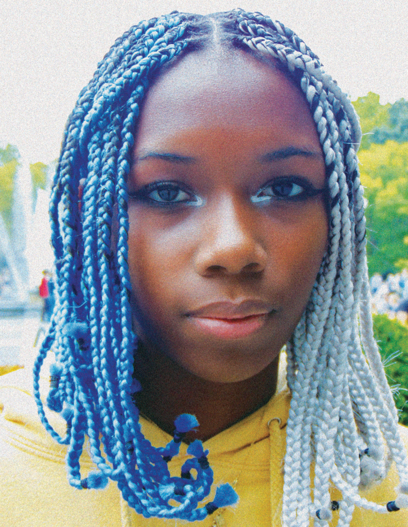 A woman with blue and grey braids in front of trees.