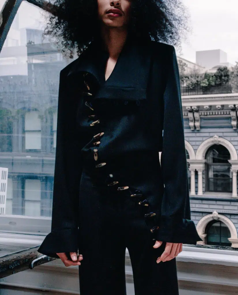 A woman in black shirt and pants standing next to window.