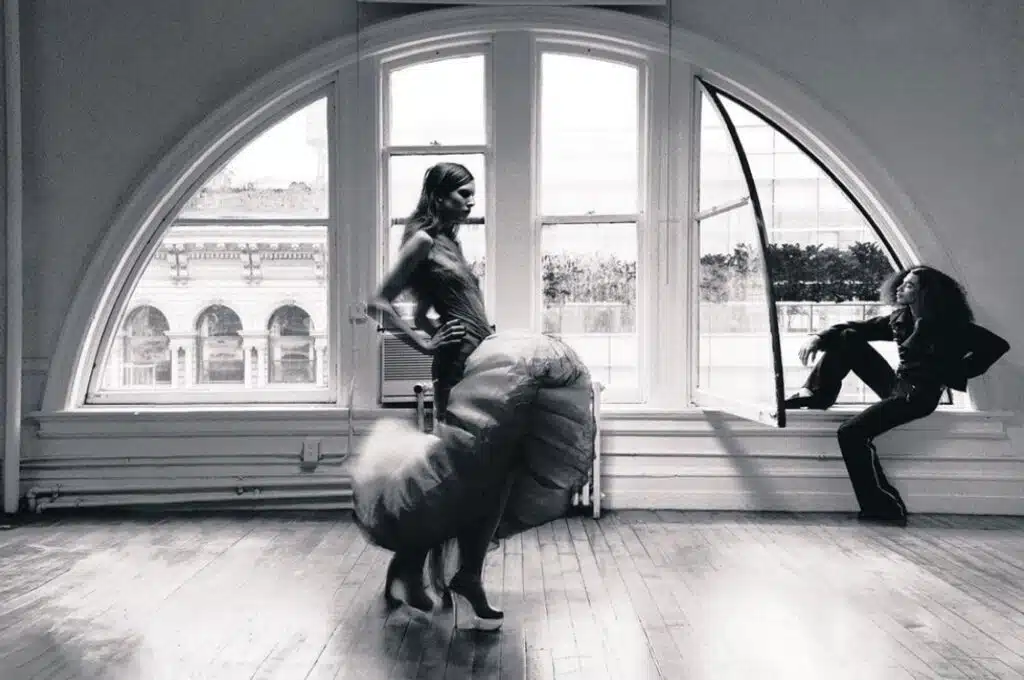 A woman standing in front of a window with two large animal heads.