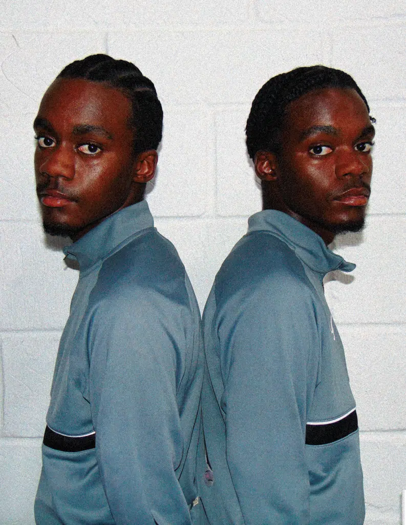 A man standing in front of a wall with his reflection in the mirror.