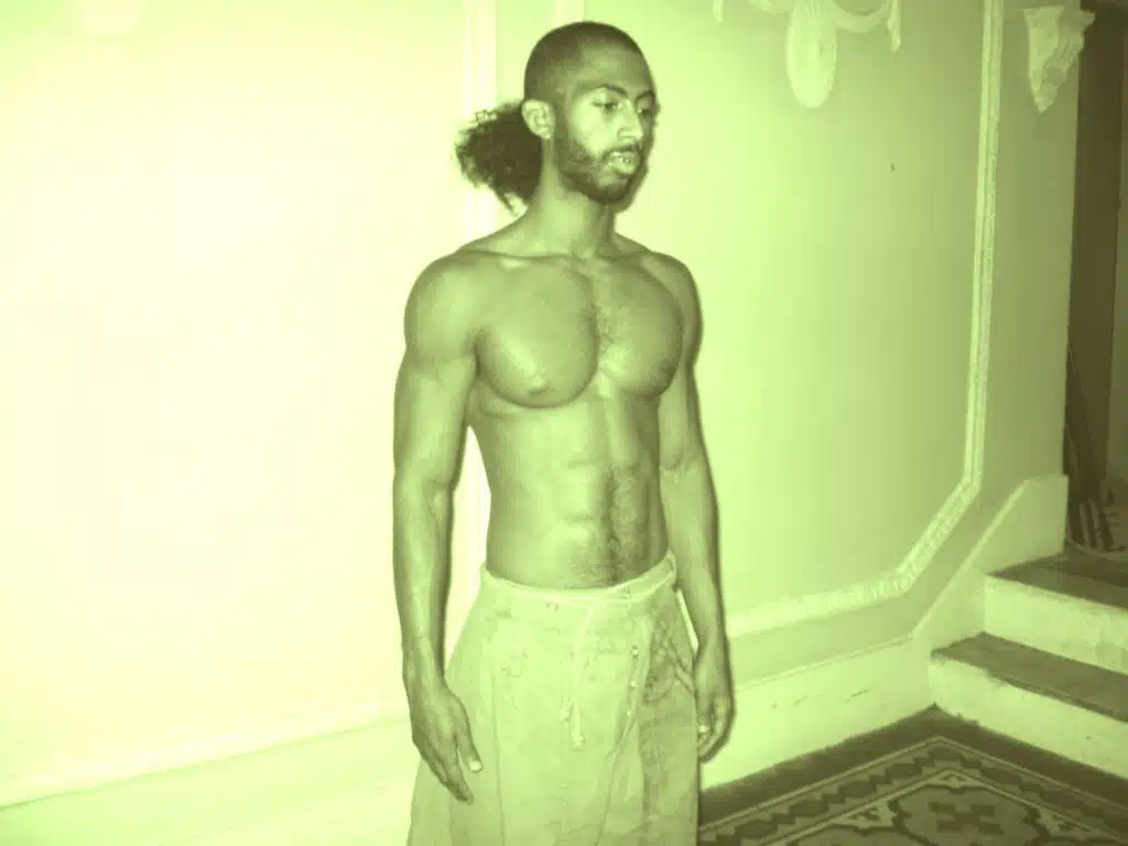 A man with no shirt standing in front of a wall.