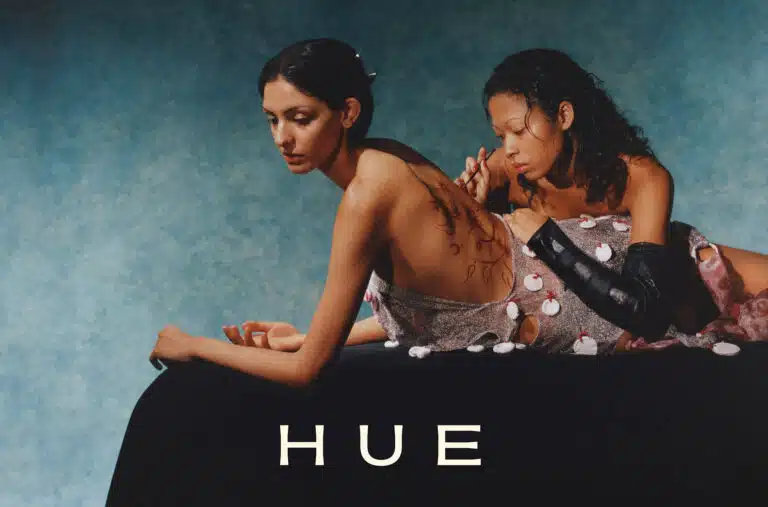 Two women sitting on a bed with the word " hue " written in front of them.